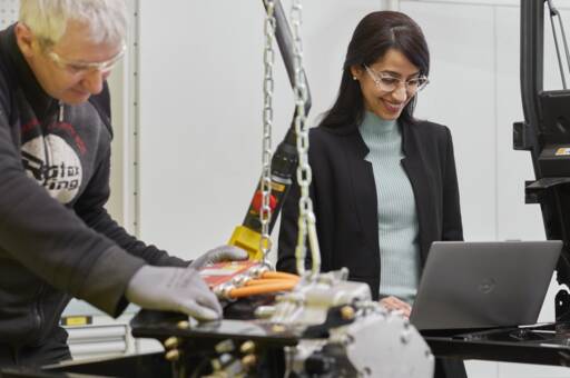 Frau arbeitet an Laptop neben Mann an Motor