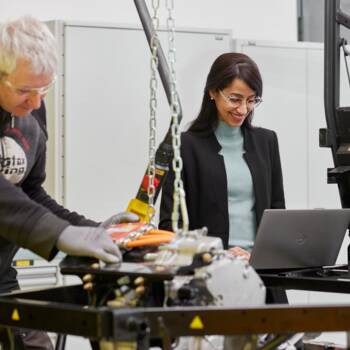 Frau arbeitet an Laptop neben Mann an Motor